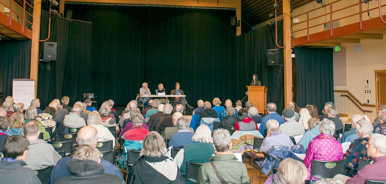 Photo Attribution: Robert S. Harrison                                Peggy Means, at the podium, Christa Campbell, Charlie Janeway and Dr. Bob Wilson addressed the clinic’s partner search, proposed public hospital district and national issues affecting our clinic.