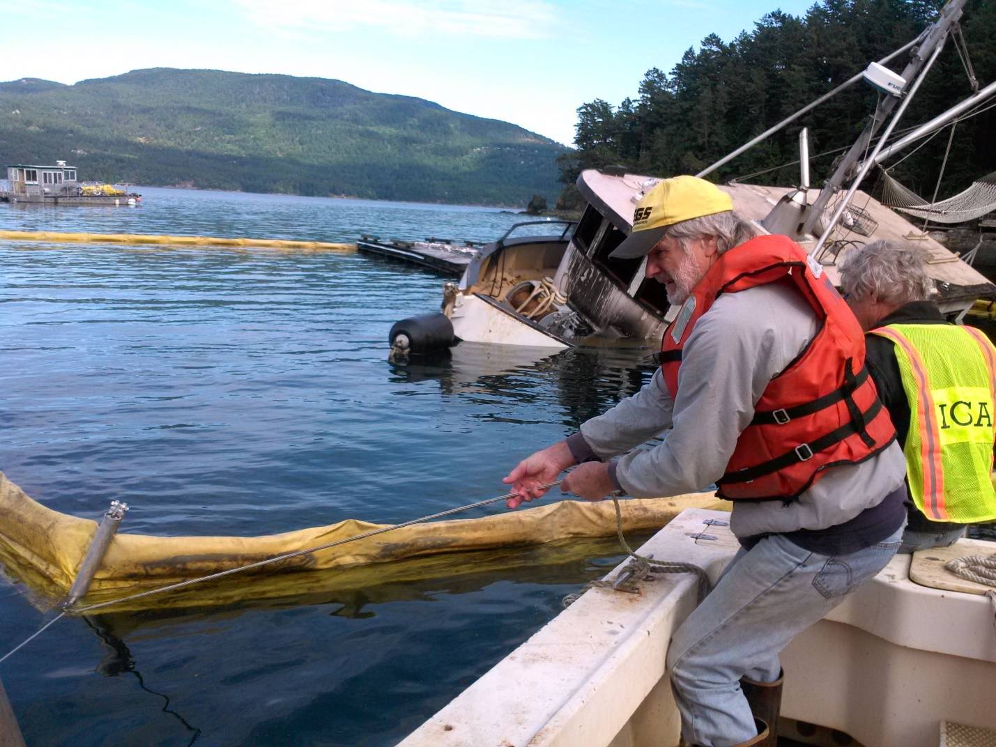 Contributed photo/ Julie Knight. Alwyn Jones and Steve Lillestol set oil containment boom around the MV Sanctuary in Judd Cove. IOSAs main response vessel, the Sea Goose, is in the background. Photo by