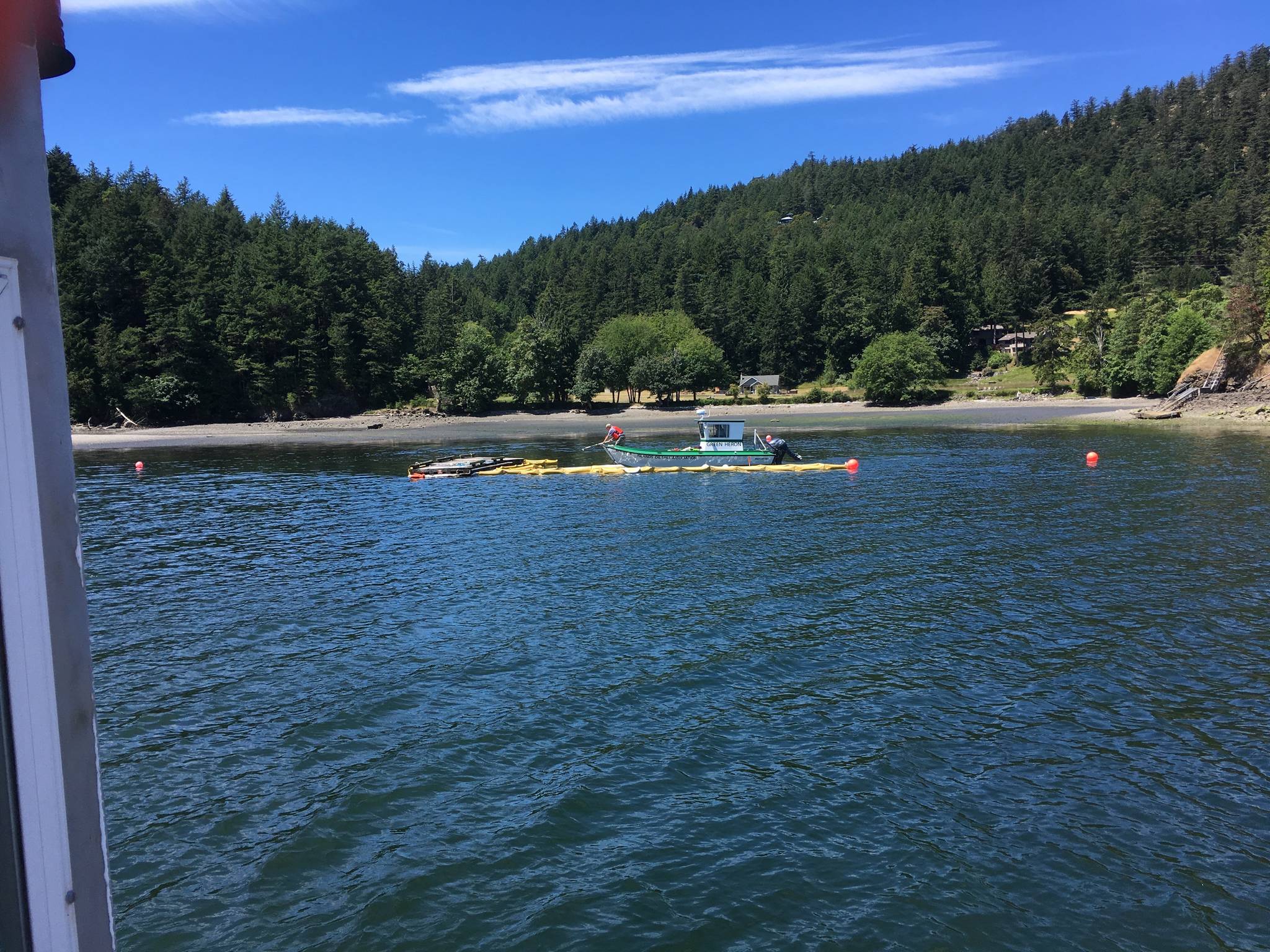 Contributed photo./ Allen Rosenberg. Jerry McElyea helps retrieve oil containment boom after the spill in Judd Cove. Ken Weatherill is driving one of IOSAs response vessels, The Green Heron.