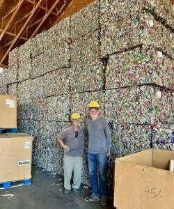 Todd Reynolds photo.
Board members John Trench (right) and Gene Helfman stand at the base of a mountain of baled aluminum cans at the Skagit River Steel and Recycling Center in Burlington. These bales are destined to become aluminum cans.